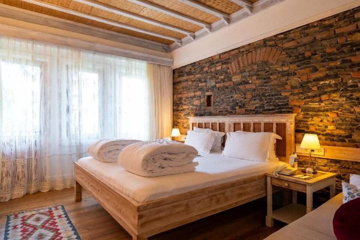 Un dormitorio con pared de piedra, una cama de madera y una mesita de noche con lámpara.