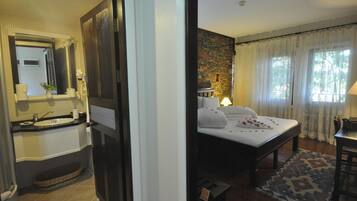 A hotel room with a bathroom and a bedroom. The bathroom has a sink, mirror, and towel rack. The bedroom has a bed, nightstand, and a window with curtains.
