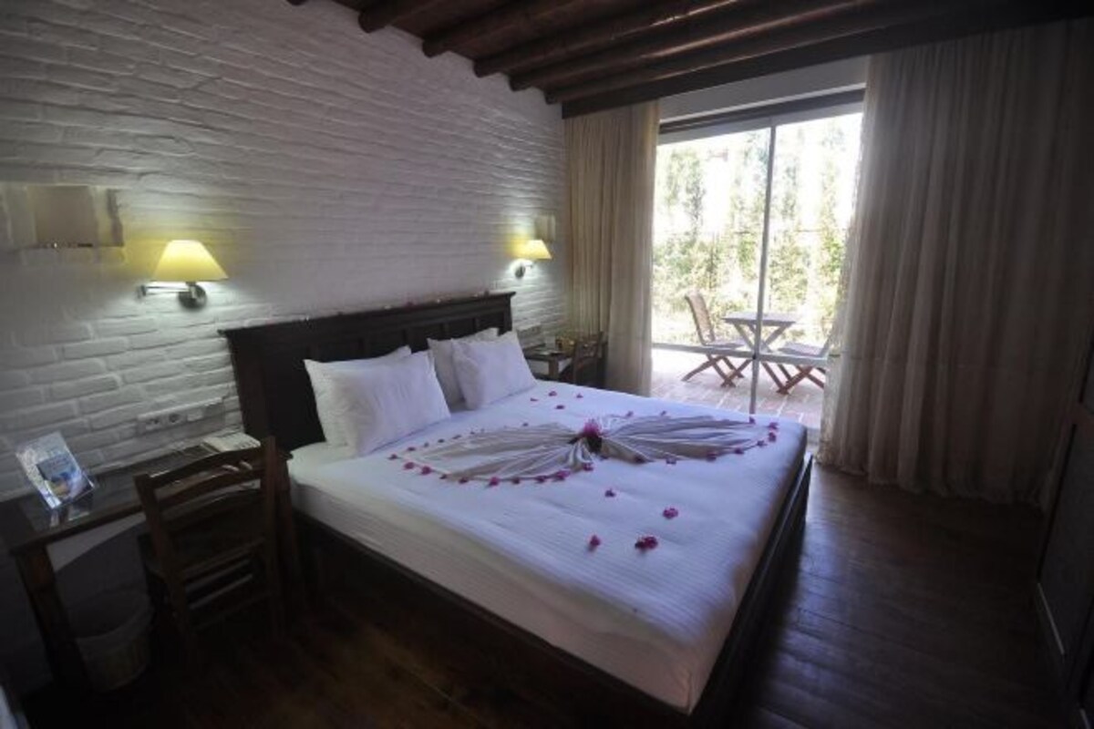 A hotel room with a large bed, two bedside lamps, a wooden headboard, and a balcony with a table and chairs.
