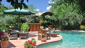 Un patio trasero con piscina, muebles de jardín y plantas en macetas.