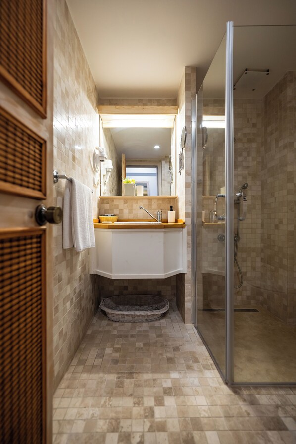 Une petite salle de bain avec une douche en verre, un lavabo blanc doté d’un plan de toilette en bois et un sol carrelé.