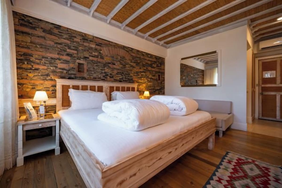 A bedroom with a stone wall, wooden bed frame, bedside lamps, and a mirror.