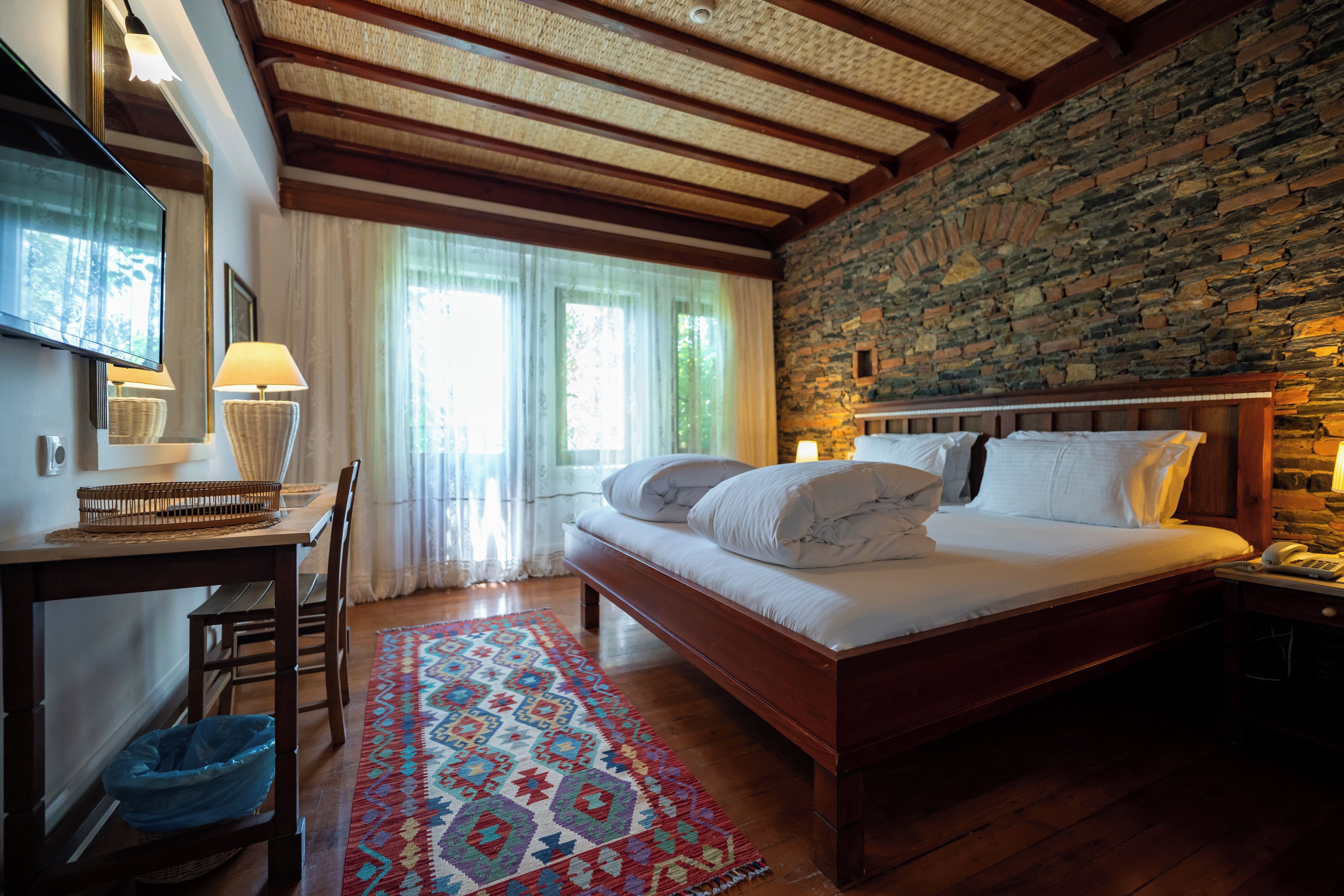 A bedroom with a wooden bed, a desk with a lamp, a telephone, and a patterned rug.