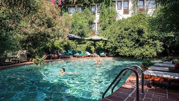 A swimming pool with clear water, surrounded by lush greenery and a building with balconies.