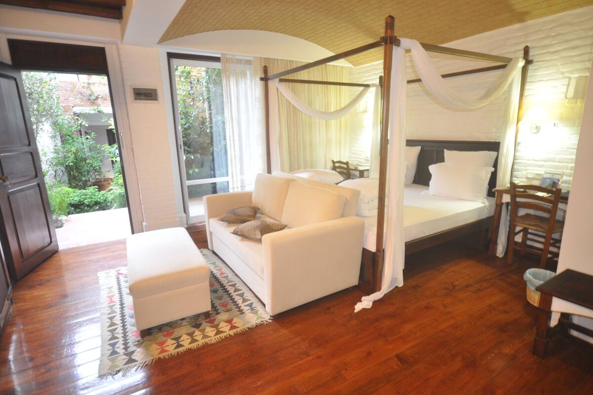 A bedroom with a four-poster bed, a sofa, and a small table.