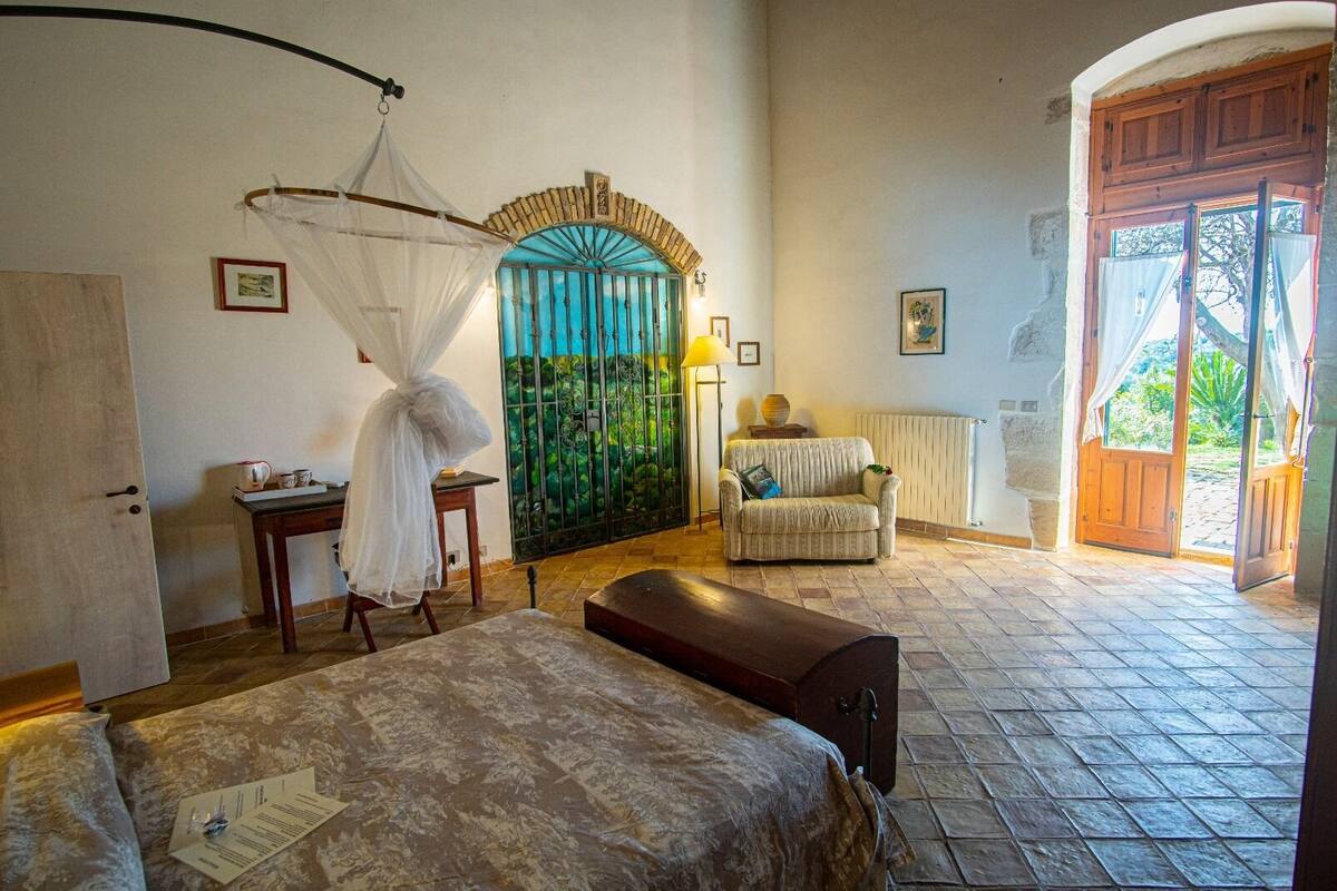 Una camera da letto con un letto, una sedia, un tavolo, una finestra vista e una porta che dà sull'esterno.