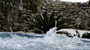 A water fountain with a stone wall and trees in the background.