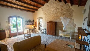 A rustic room with a stone wall, wooden furniture, a cot, and a view through a glass door.
