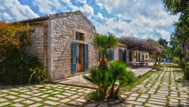 A stone building with a tiled courtyard, a palm tree, and a view of the sky.