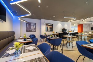 A modern dining area with blue seating, tables with place settings, and a coffee station.