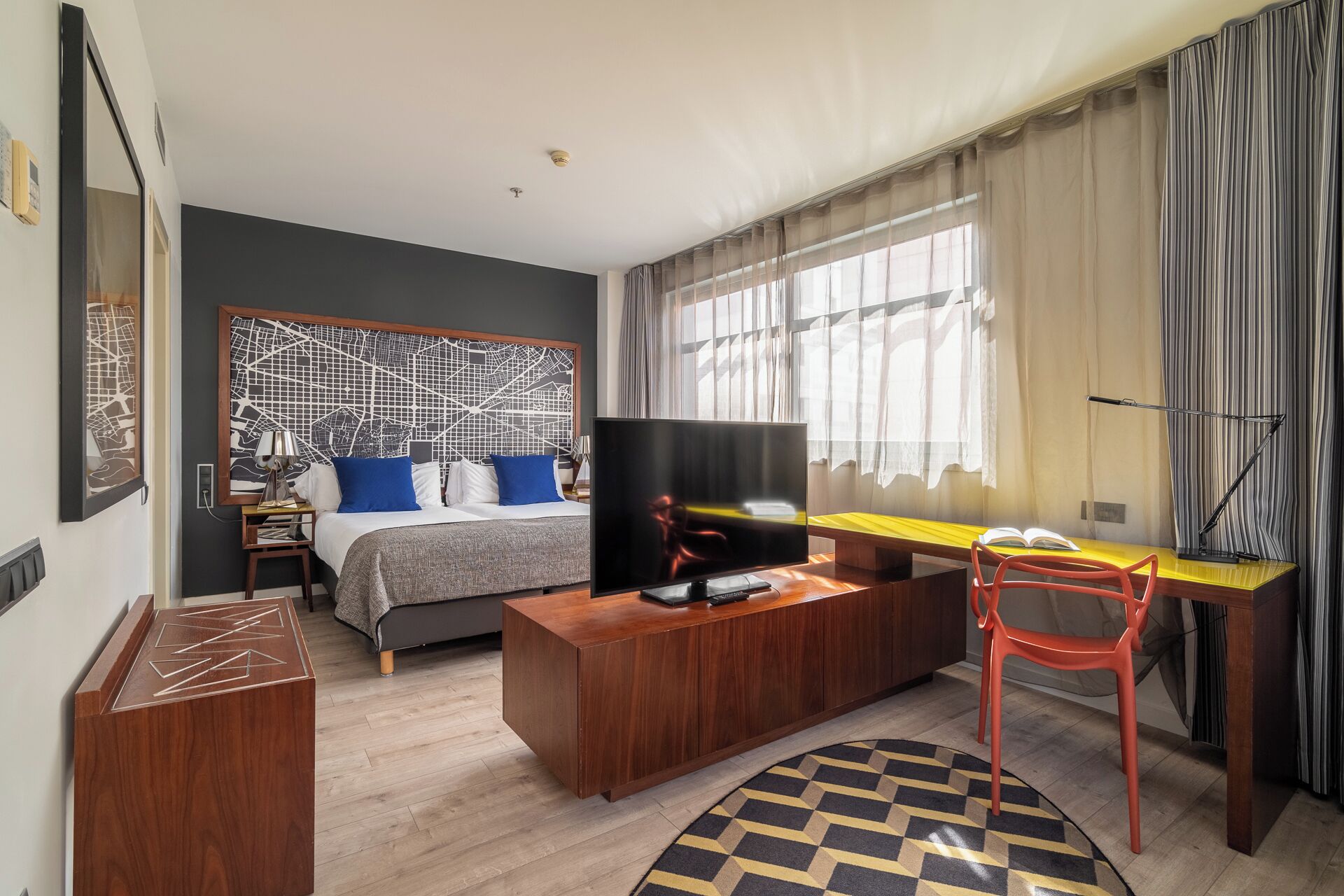 A modern hotel room with a bed, a desk, a TV, and a chair.