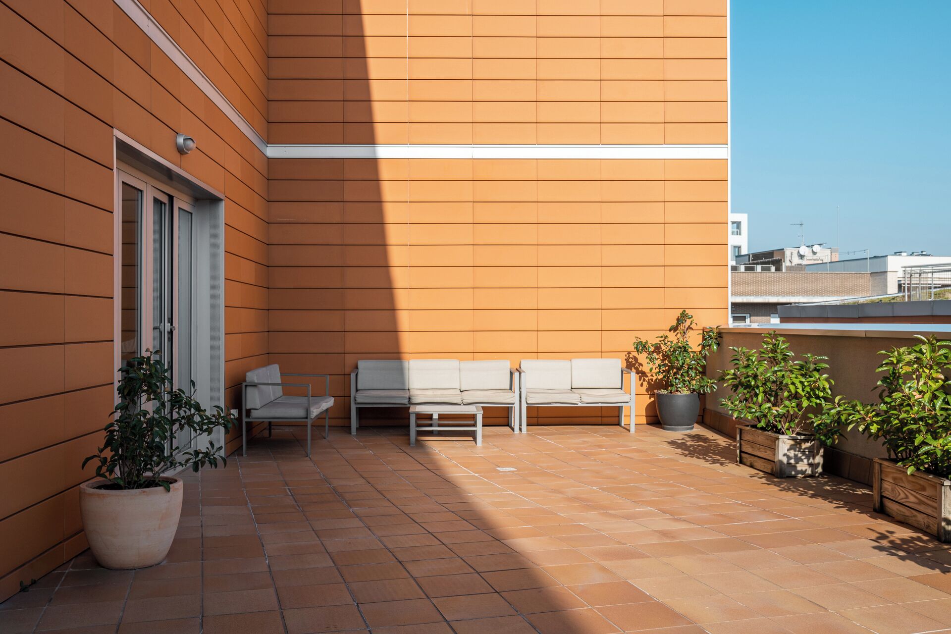A modern outdoor seating area with a tiled floor, a white bench, and potted plants.
