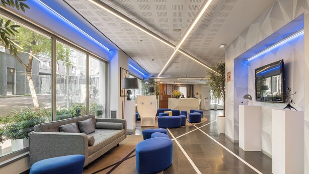 A modern lobby with a reception desk, seating areas, and large windows offering views of the street. - Naitly Barcelona Poblenou (Barcelona)