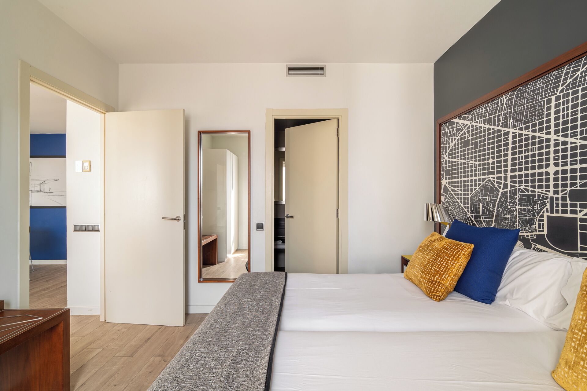 Une chambre d’hôtel avec un lit, un bureau en bois, une armoire et une salle de bain visible à travers une porte ouverte.