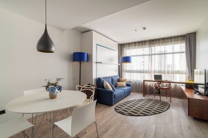 A modern living room with a round dining table, a blue sofa, and a TV on a wooden cabinet.