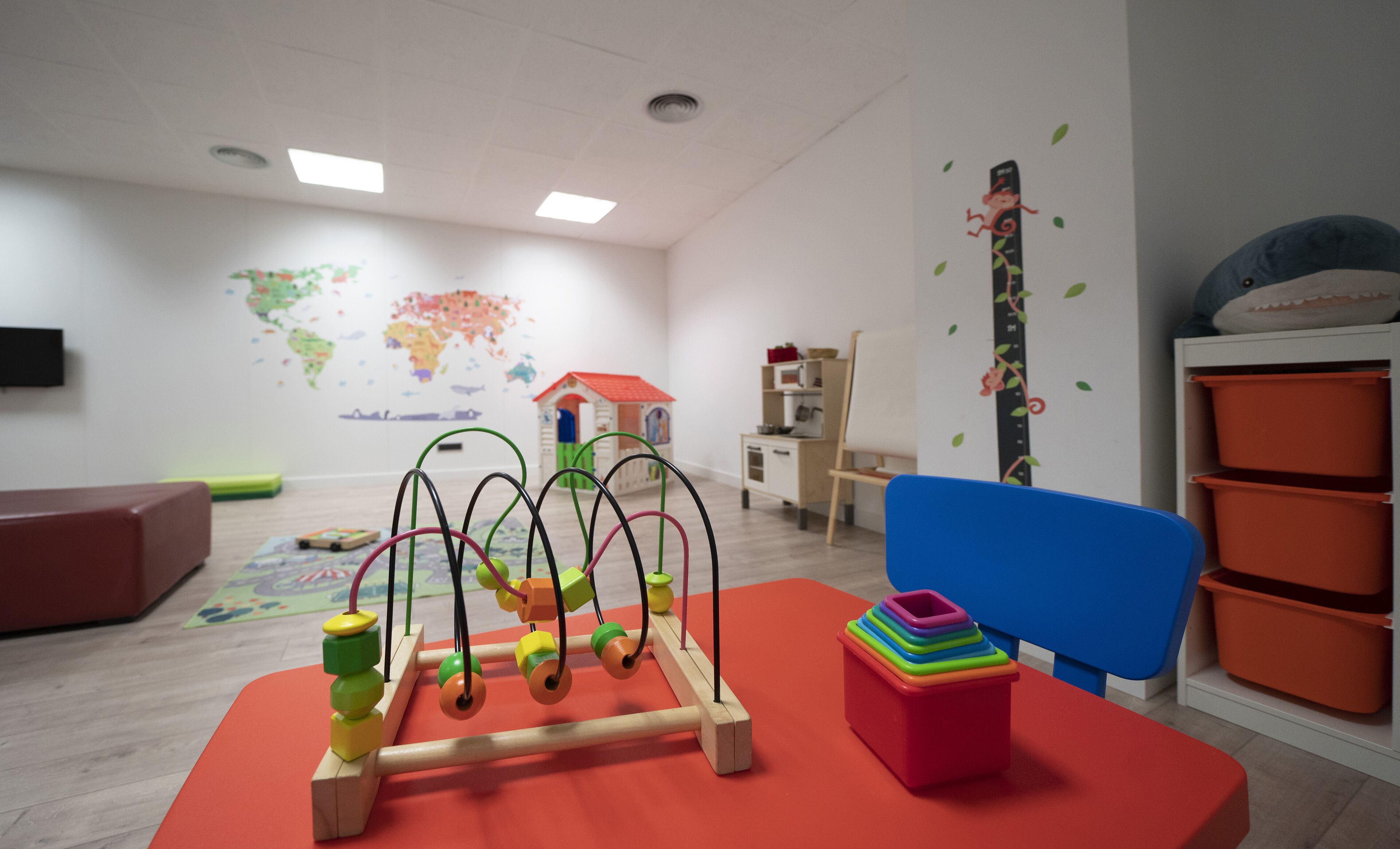 A playroom with a wooden bead maze, colorful storage bins, a world map mural, and a small house playhouse.