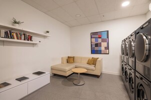 A laundry room with a beige sofa, a small round table, and a bookshelf with books.