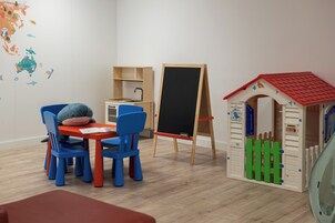 A children's playroom with a small table, chairs, a playhouse, and a chalkboard.