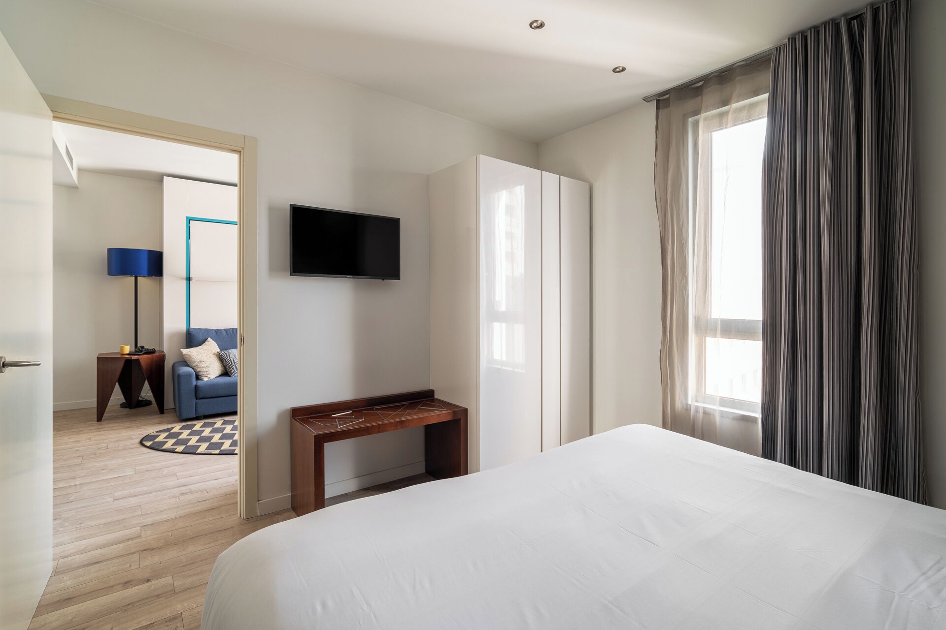 A hotel room with a large bed, a TV mounted on the wall, a desk, and a wardrobe.
