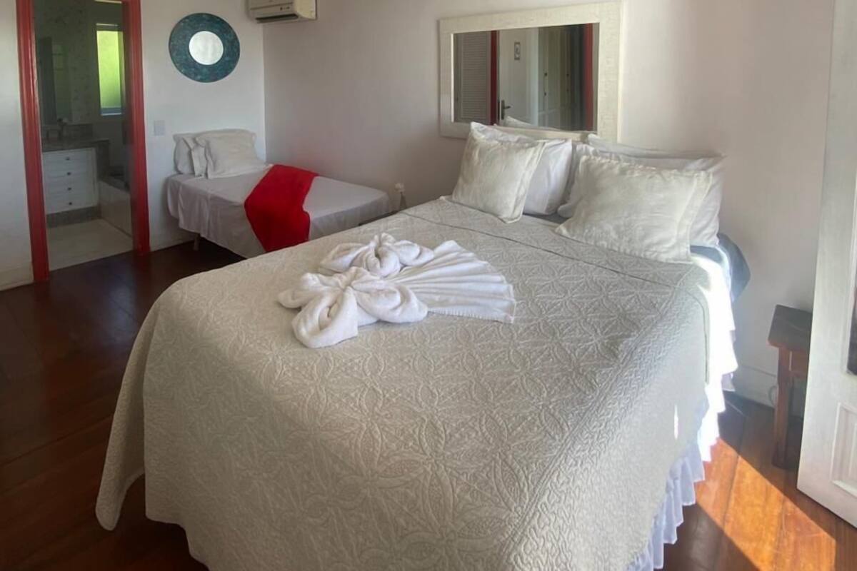 Une chambre d’hôtel avec un lit, un ventilateur de plafond, un miroir rond et une chaise rouge.