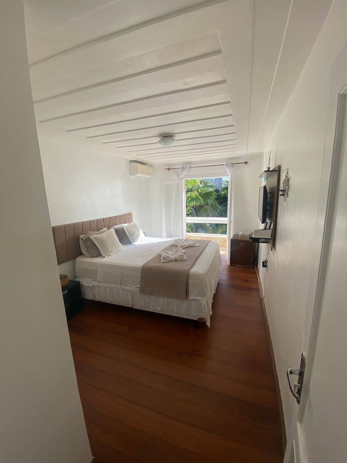 Un dormitorio con cama, ventilador de techo, ventana con cortinas y vista a zonas verdes.