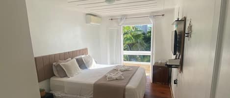 Un dormitorio con cama, ventilador de techo, ventana con cortinas y vista a zonas verdes.