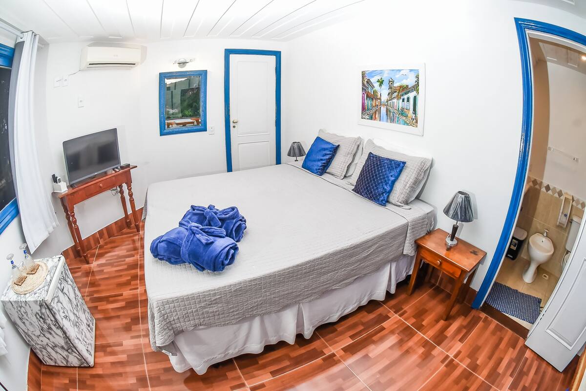 Une chambre avec un grand lit, une télévision, une petite table et une porte menant à la salle de bain.