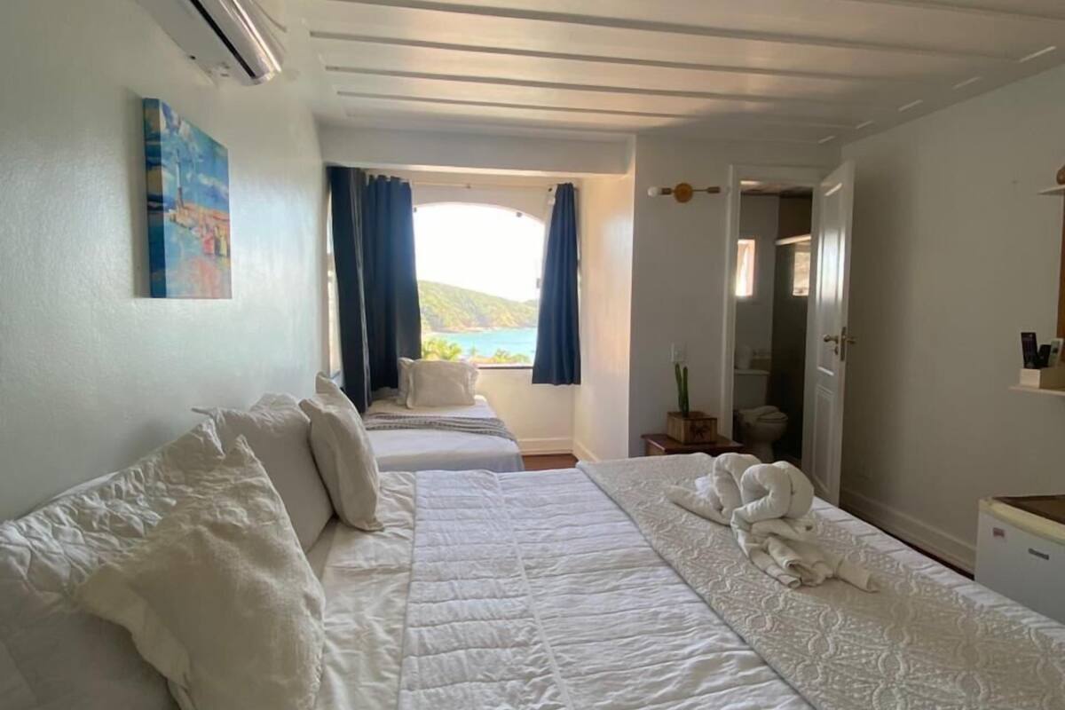 Une chambre d’hôtel avec deux lits, un tableau au mur, un appareil de climatisation et une vue sur la mer par la fenêtre.