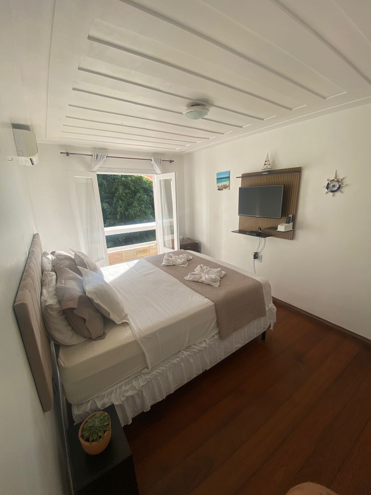 Une chambre à coucher avec un lit, une télévision, une fenêtre et un ventilateur de plafond.