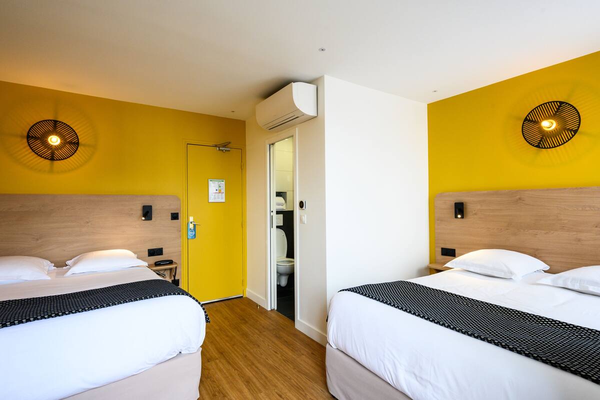 A hotel room with two beds, a wooden headboard, a yellow accent wall, and a ceiling fan.