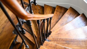 Un escalier en colimaçon en bois, doté de balustres en métal et d’une main courante.