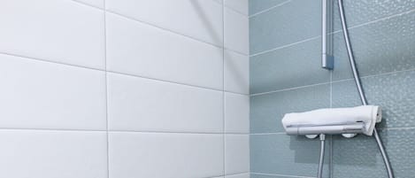 A bathroom with white and teal tiles, a showerhead, and a towel rack.