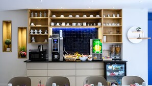 Un espace moderne dédié au petit-déjeuner, équipé d’une machine à café, d’un panier de fruits et d’un réfrigérateur rempli de boissons.