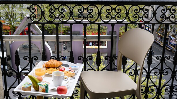 Un balcon avec une chaise et un plateau contenant divers éléments pour le petit-déjeuner, notamment des croissants et du jus.