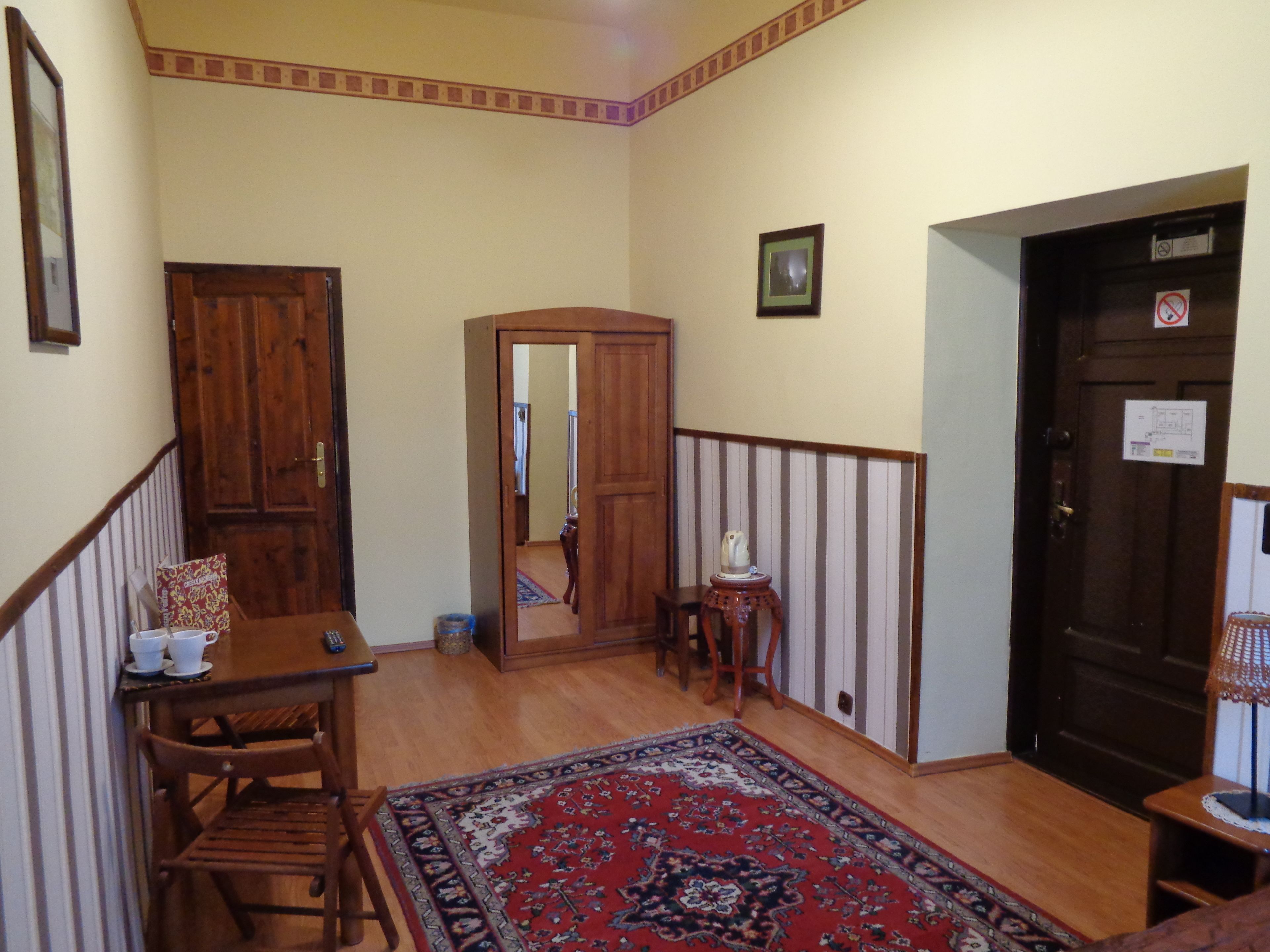 A hallway with a wooden staircase, a dining area with a table and chairs, a patterned rug, and a door with a no-smoking sign.