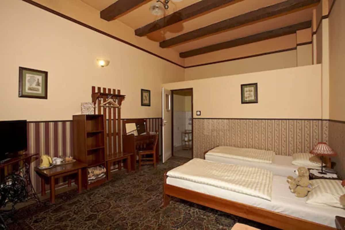 A hotel room with two beds, a wooden wardrobe, a desk with a chair, a television, and a lamp.