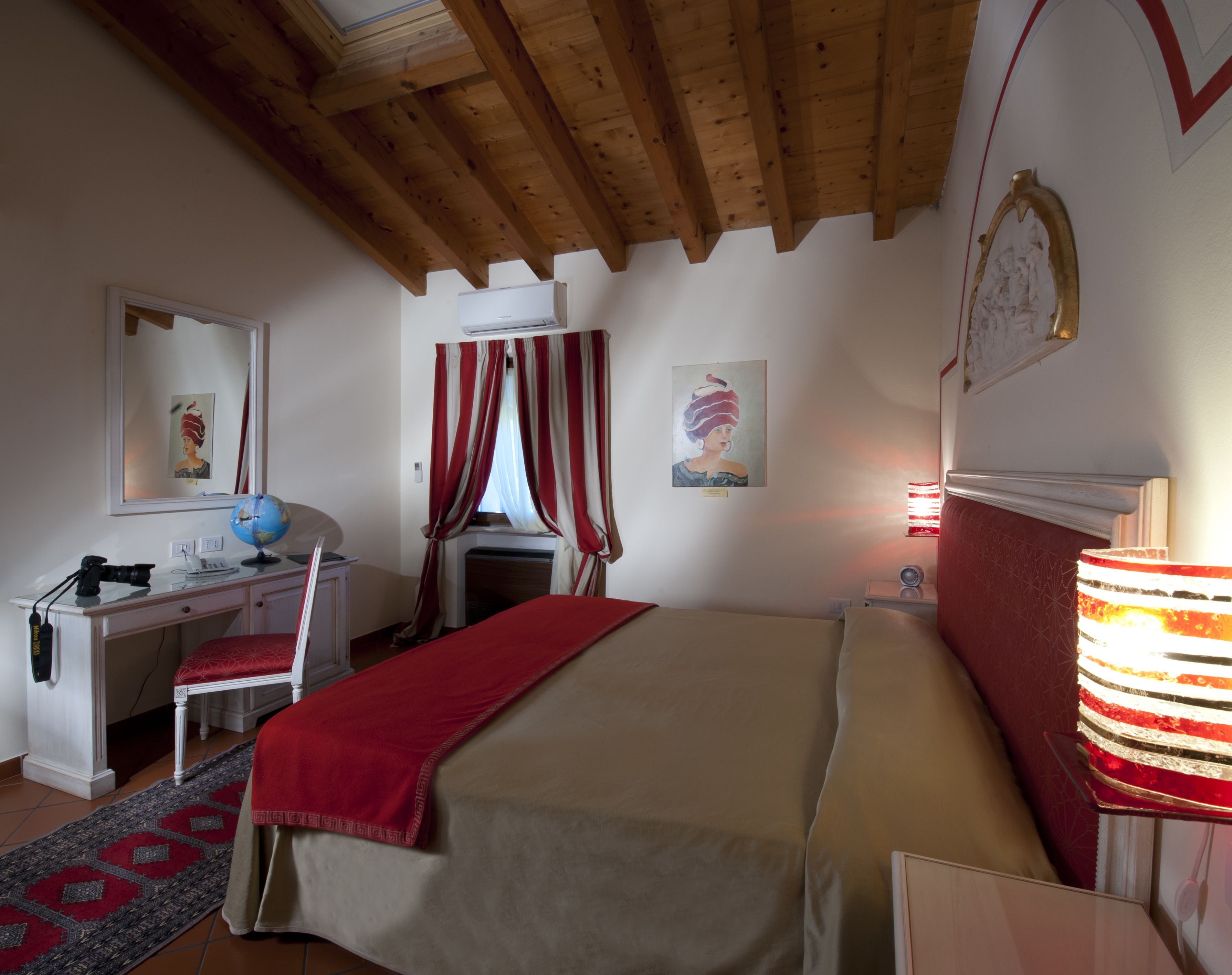 A bedroom with a bed, a desk with a globe, a chair, a lamp, and a window with curtains.