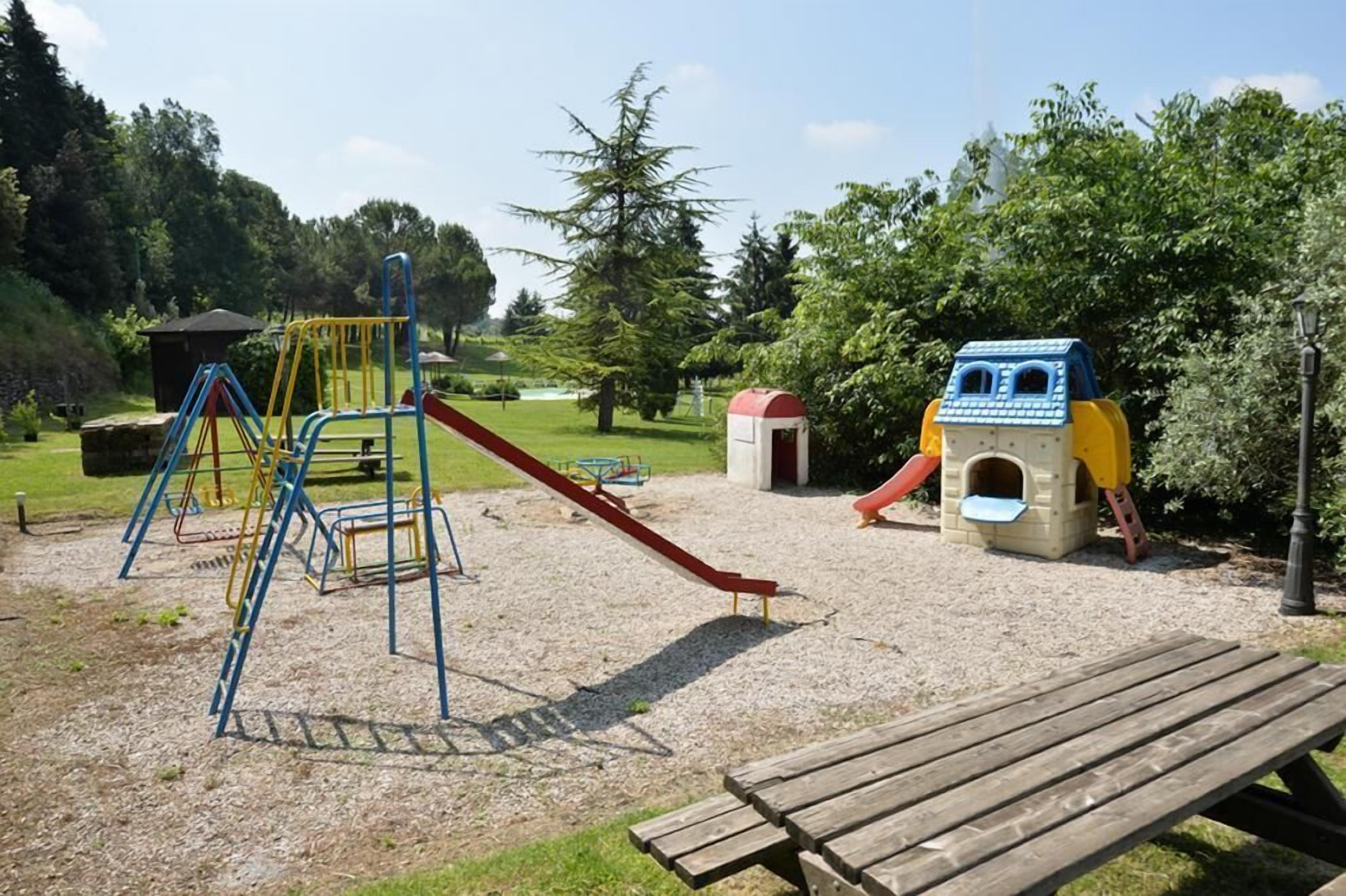 A playground with a slide, climbing structures, and a small house-like playhouse.