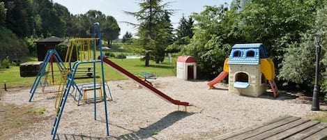 A playground with a slide, climbing structures, and a small house-like playhouse.