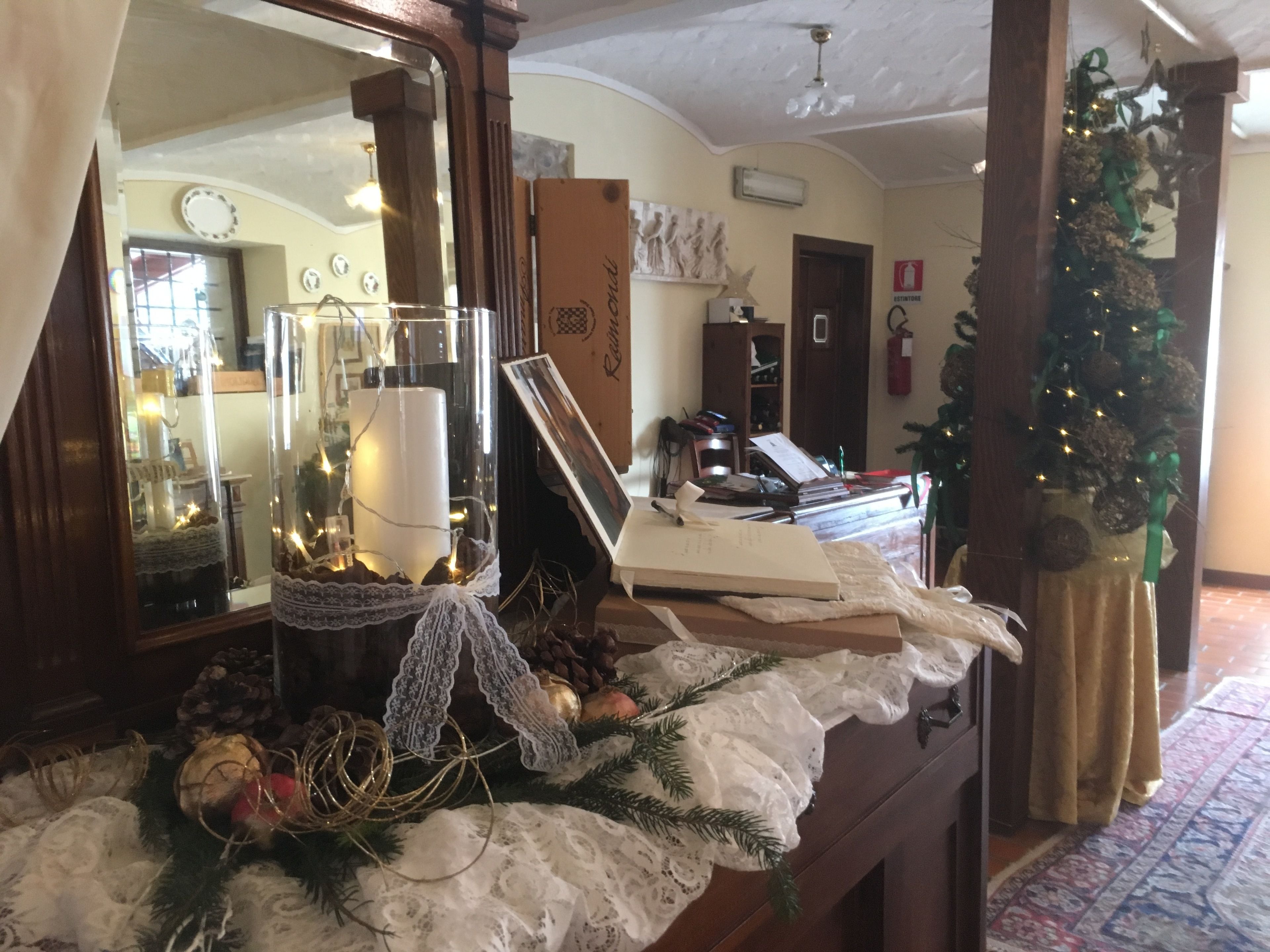 Une pièce avec une commode en bois, un miroir et un sapin de Noël. Un tableau encadré est appuyé contre la commode, et une petite table porte une bougie et des décorations.