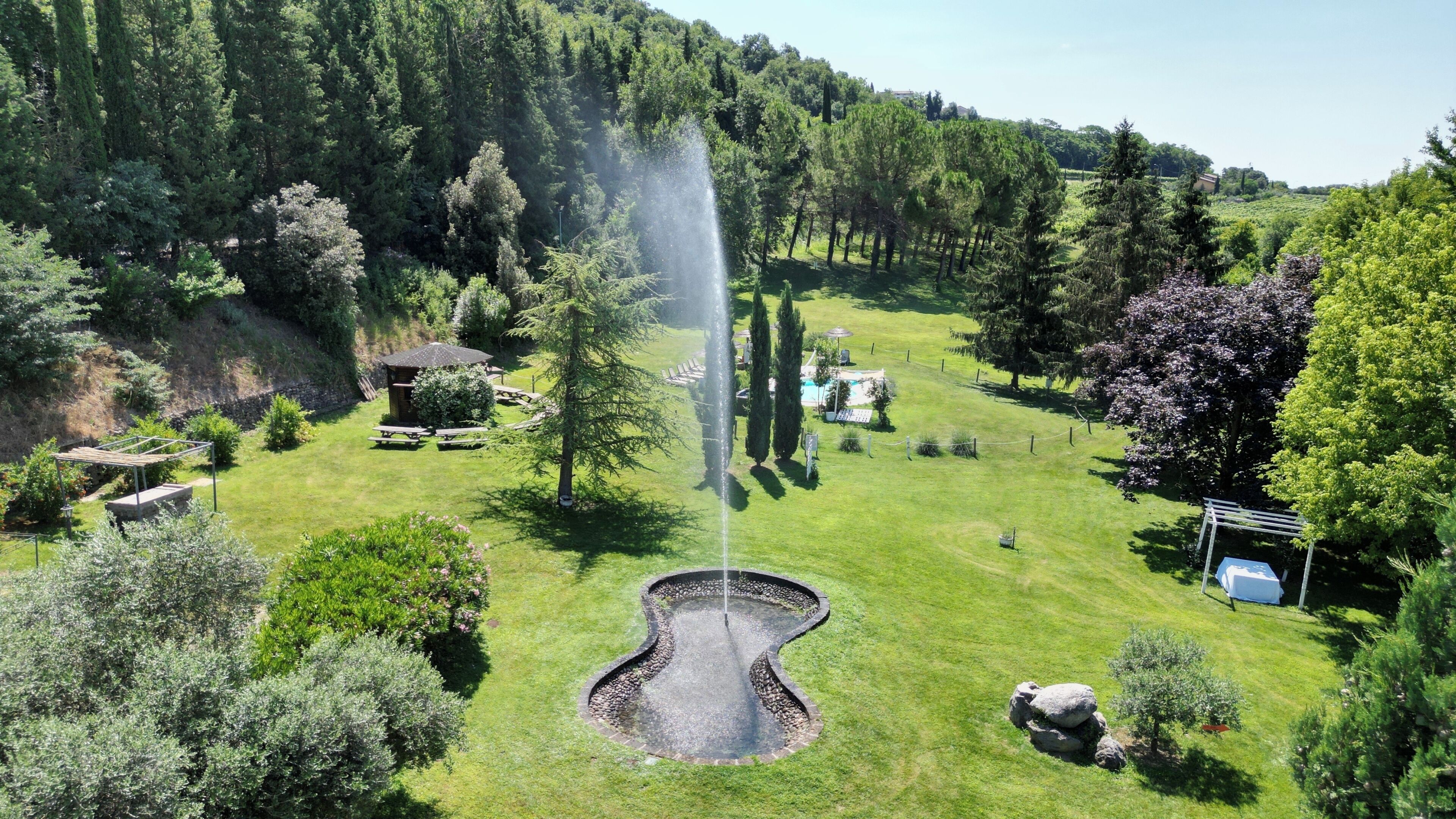 Un jardín ajardinado con una fuente, mesas de picnic y una piscina.