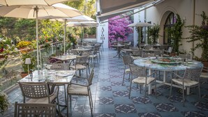 An outdoor cafe with tables and chairs, surrounded by potted plants and flowers. - Hotel Fontermosa (Orbetello)