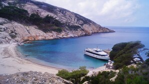 A coastal scene with a yacht docked near a rocky beach and a clear view of the sea. - Hotel Fontermosa (Orbetello)