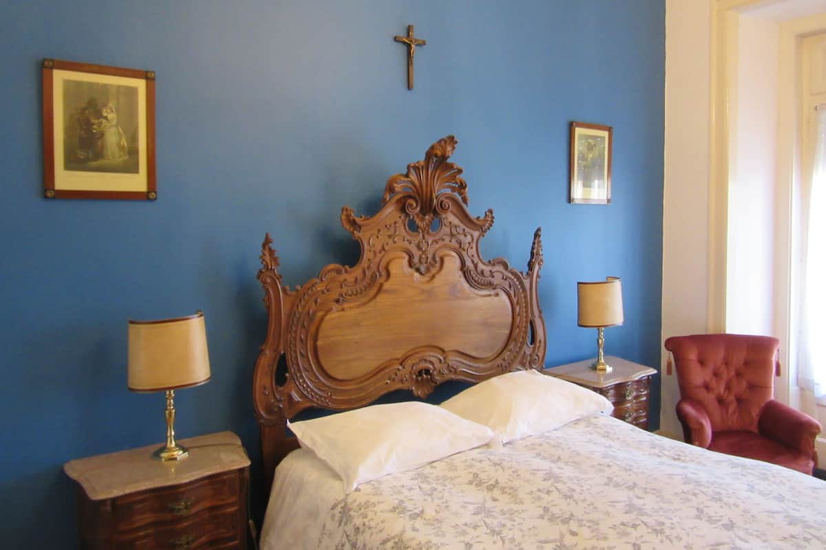Une chambre à coucher avec un grand lit en bois, deux tables de chevet avec des lampes, un fauteuil rouge et deux tableaux encadrés accrochés au mur.