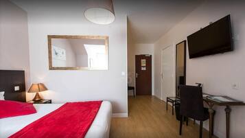 A hotel room with a bed, a desk, a chair, a TV, a mirror, and a door leading to another room.