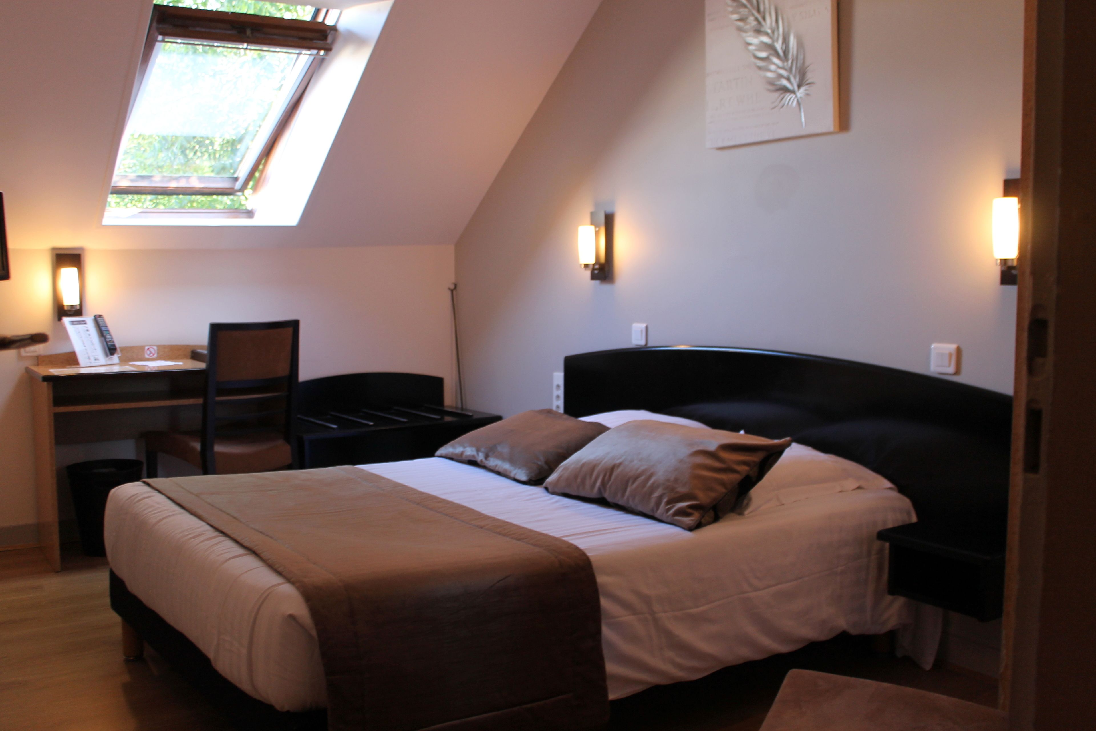 Une chambre à coucher avec un lit, un bureau et une chaise. Il y a une lucarne au-dessus du bureau.