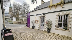 A building with a stone facade, a purple sign, and potted plants. - Hotel Le Bayeux (Bayeux)