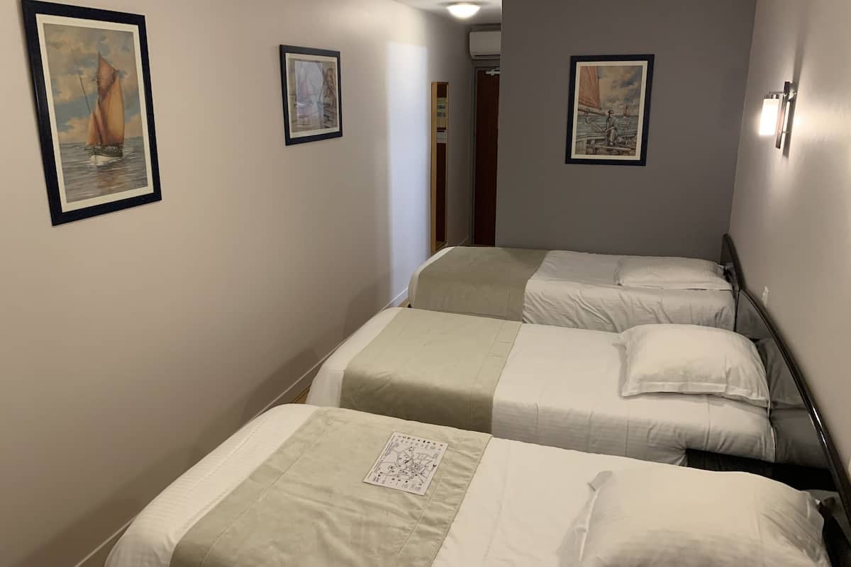 Une chambre d’hôtel avec deux lits simples, un petit bureau et une chaise. Les murs sont ornés de tableaux encadrés.
