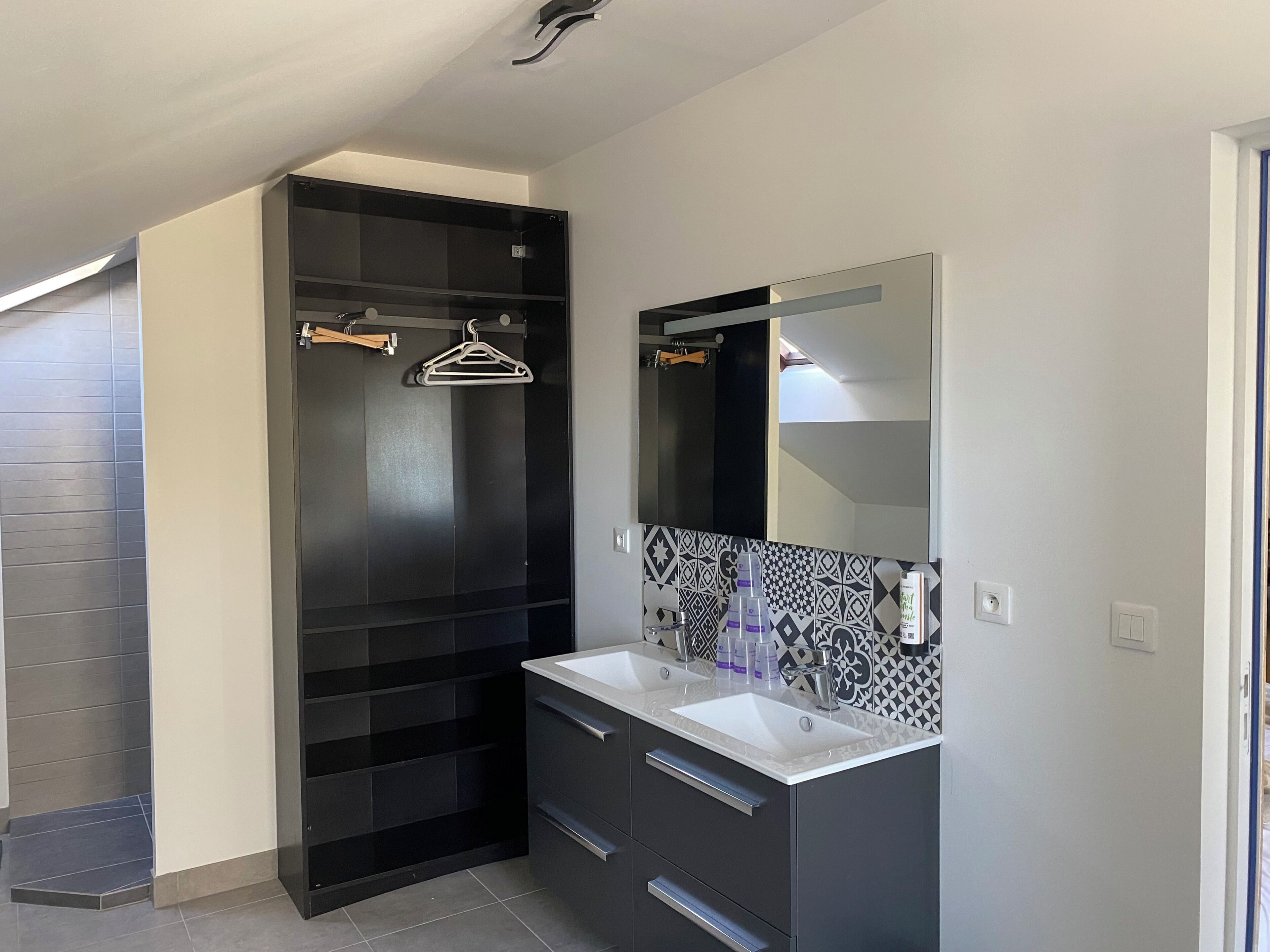 A modern bathroom with a black vanity, two sinks, a large mirror, and a hanging clothes rack.