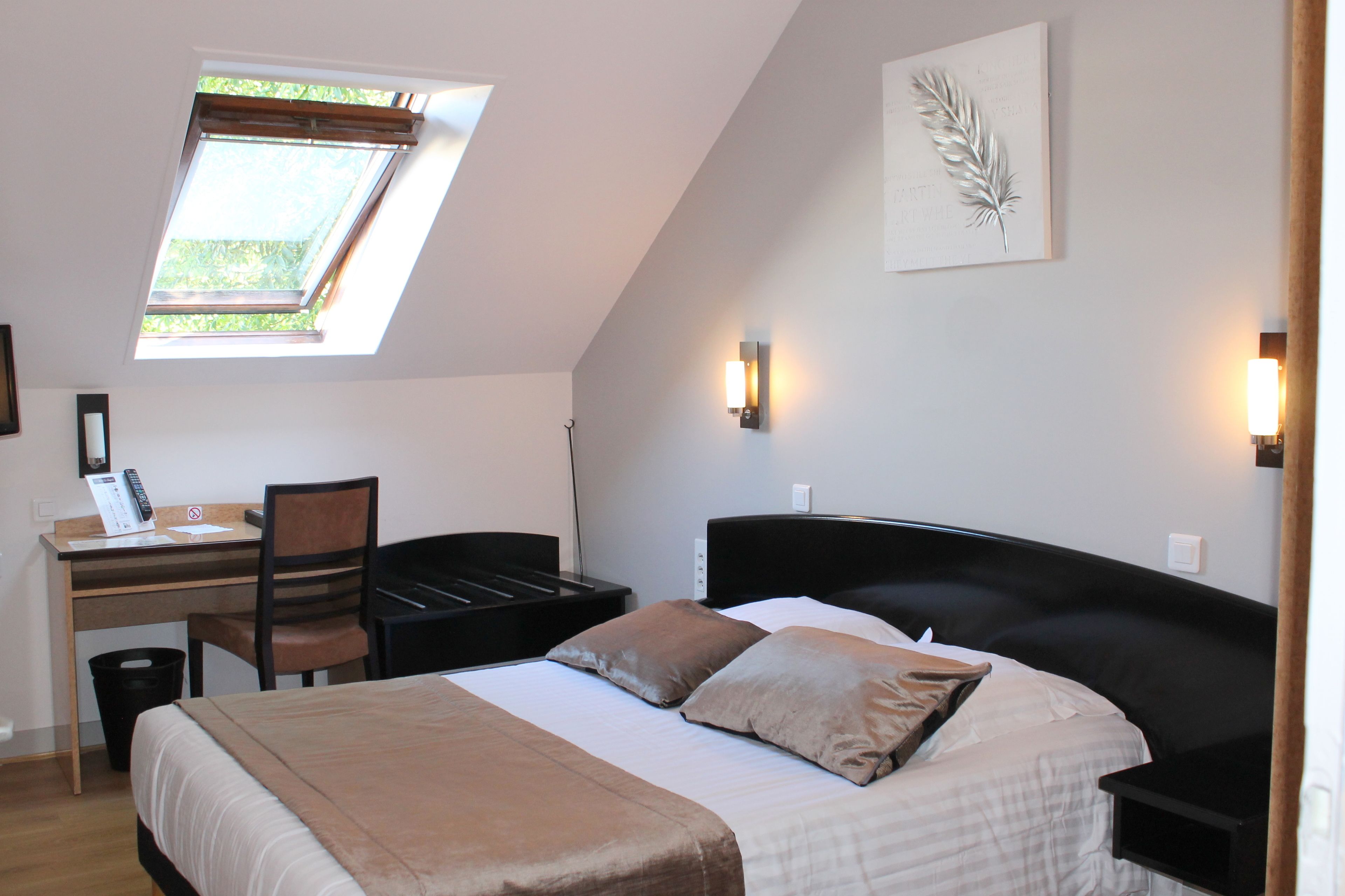 A bedroom with a bed, desk, and chair. There is a skylight above the desk and a wall-mounted light fixture.